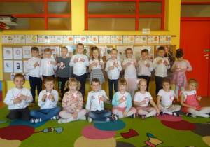 Grupa dzieci trzyma przyłożony do klaski piersiowej kotylion z papieru.